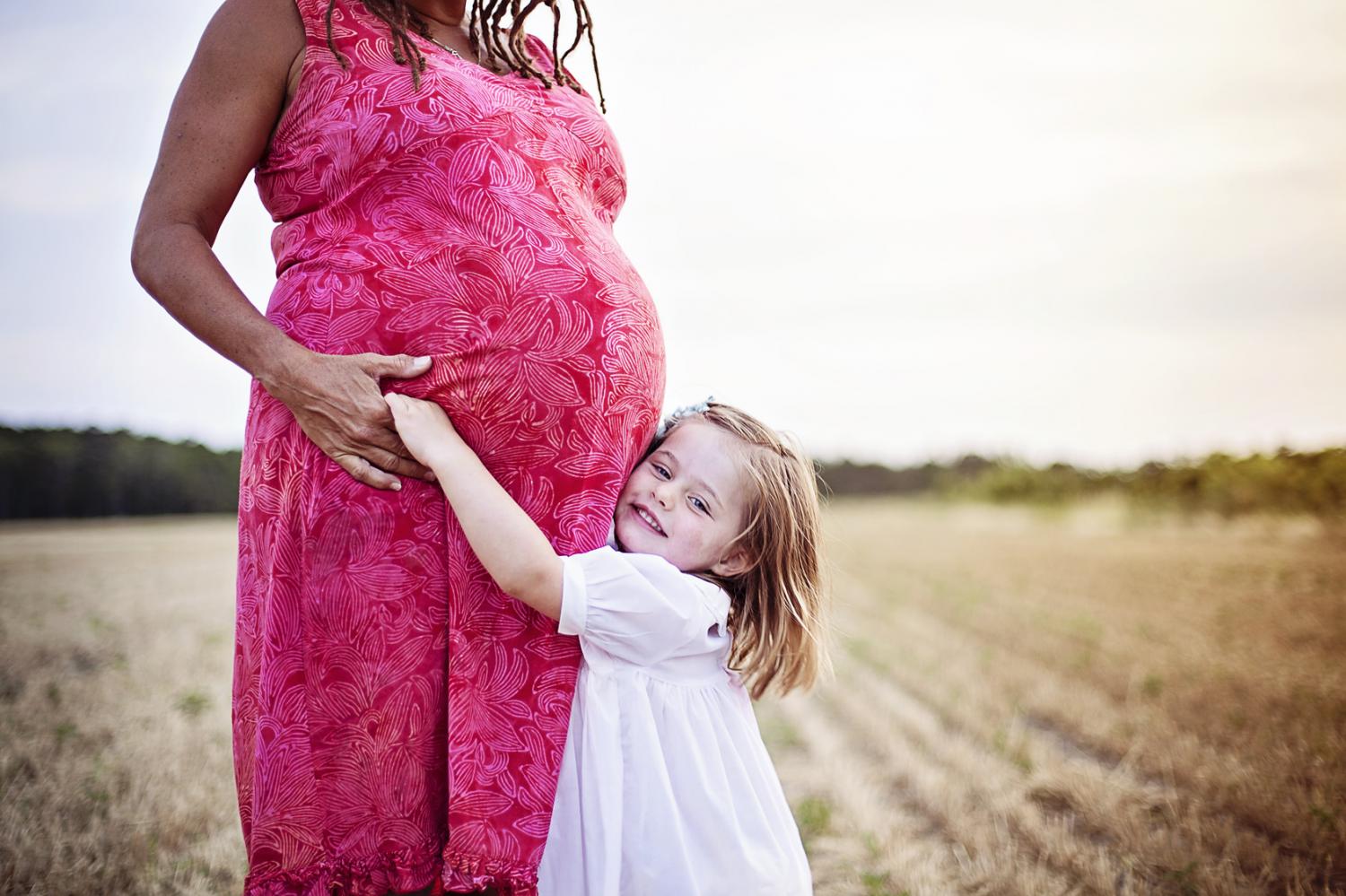 Daughter hugging mom's pregnant belly in field by the Weeping Radish in NC